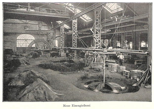 Schwarzes und weißes Foto einer frühen deutschen Fabrik mit Arbeitern, die an Maschinen arbeiten, umgeben von Metallstangen und -pfählen, beschriftet mit "Neue Eisenglebeerei, die erste Fabrik in Deutschland" unten.