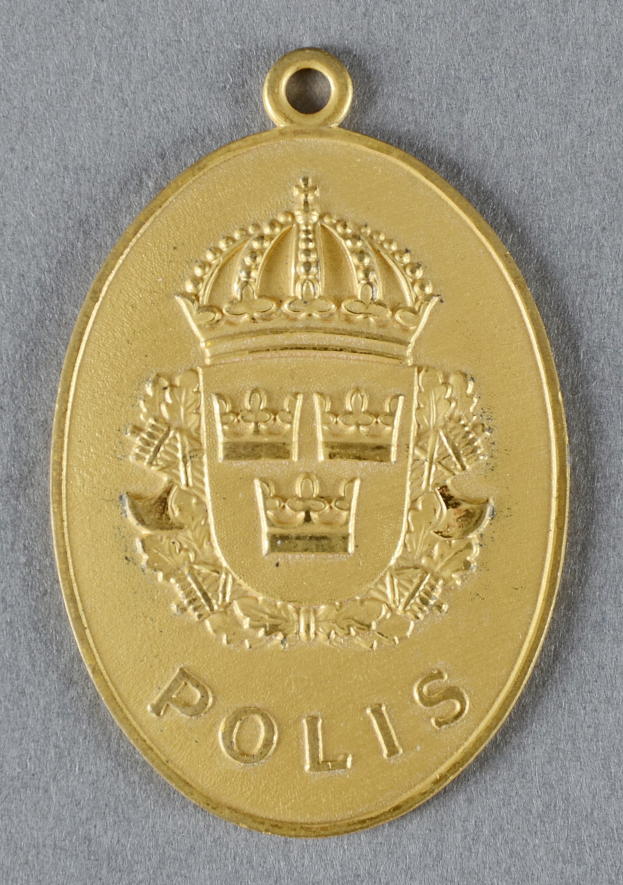 Goldene Medaille mit einer Kroneförmigen Polizeimarke in der Mitte, mit eingravierter Schrift.
