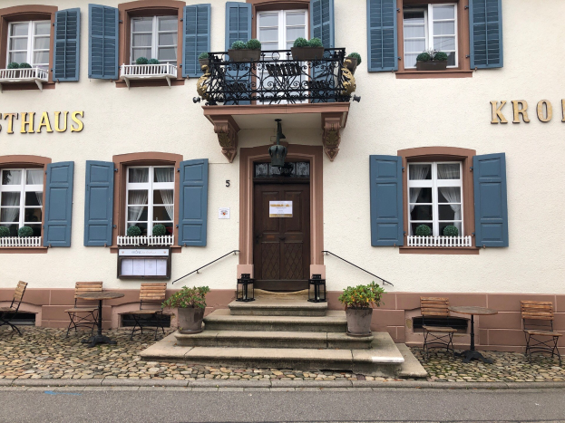 Ein zweistöckiges Gebäude mit blauen Fensterläden, Fenstern, Türen, Geländern, Topfpflanzen, Tischen, Stühlen, Treppen und einer Straße in Sthaus, Deutschland.