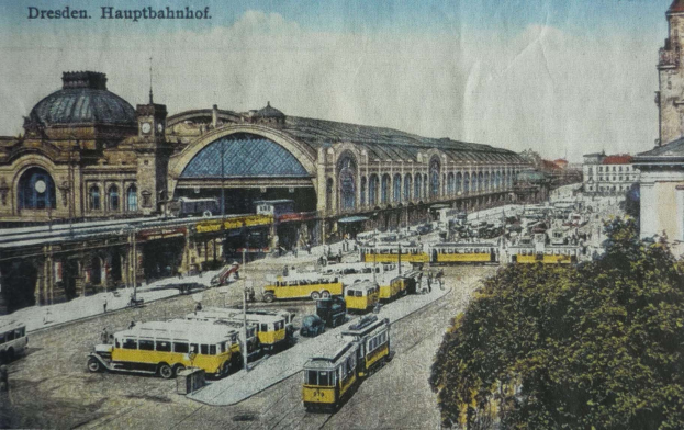 Eine alte Postkarte zeigt den Dresdner Hauptbahnhof in Dresden, Deutschland, mit einer belebten Straßen- und Fußgängerszene, Bäumen, Gebäuden und einem bewölkten Himmel.