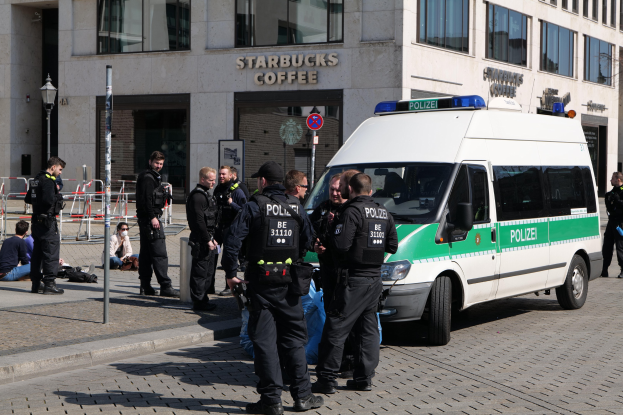 Polizeibeamte vor einem Starbucks-Café mit einem Van auf der rechten Seite und Menschen auf der linken Seite, im Hintergrund ein Gebäude, ein Schild, eine Straßenlaterne und ein Zaun.