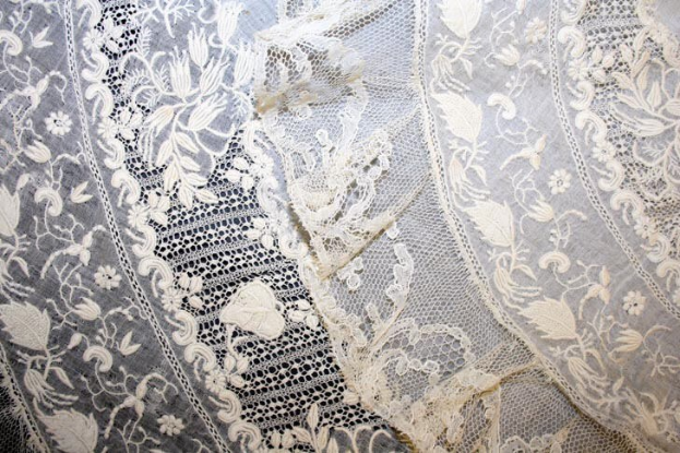 Nahaufnahme eines weißen Hochzeitskleids mit zarter, kunstvoller Spitzenverzierung mit verschiedenen Mustern auf einem leichten, luftigen Stoff.