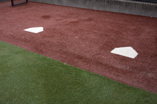 Baseballfeld mit Kunstrasen, einem Zaun, Home Plate in der Mitte und einer Wand im Hintergrund.