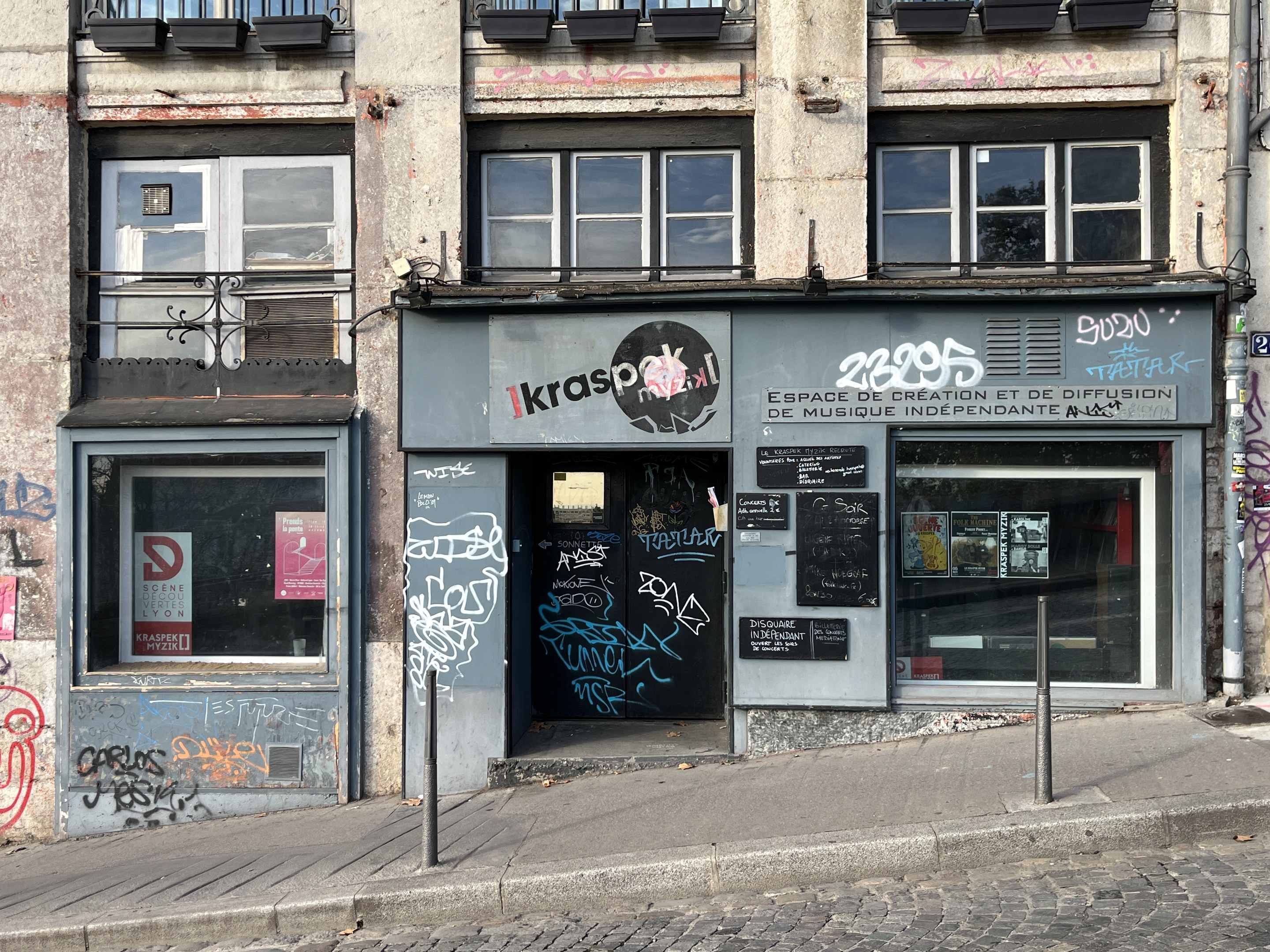 Gebäude mit Fenstern, Geländern, Türen, Plakaten und Graffiti an der Seite, das über einer Straße liegt.