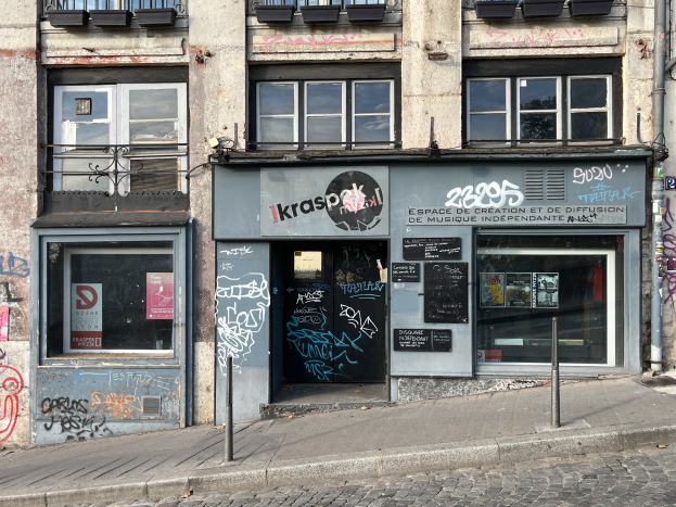 Gebäude mit Fenstern, Geländern, Türen, Plakaten und Graffiti an der Seite, das über einer Straße liegt.