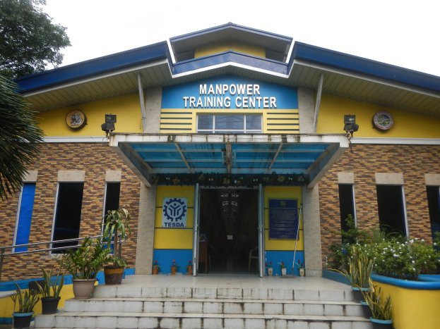 Außenansicht des Manpower Training Center in Manila, Philippinen, mit Treppe, Topfpflanzen, einem Baum und einem Gebäude mit Fenstern, Türen und Beschriftungen.