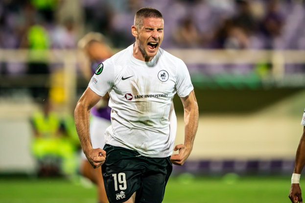 Ein Mann in einem weißen Hemd und schwarzen Shorts rennt auf einem Fußballfeld, umgeben von einer Gruppe von Menschen, die ein Tor während eines Spiels zwischen Leeds United und Melbourne Victory feiern.