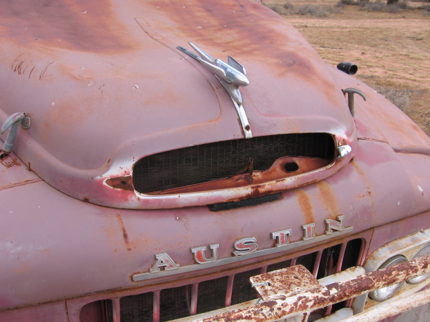 Ein rostiges, altes LKW steht in einem Feld mit Bäumen und einem klaren blauen Himmel, zeigt Anzeichen von längerer Witterungseinwirkung.