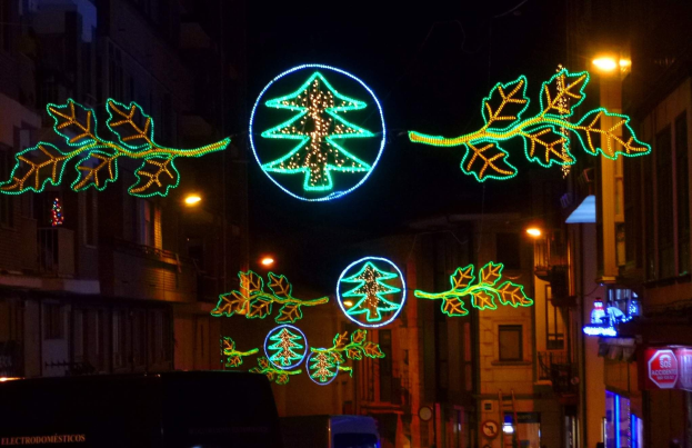 Eine städtische Straße, die mit festlichen Weihnachtslichtern in Form von Blättern geschmückt ist, mit fahrenden Fahrzeugen und Gebäuden auf beiden Seiten.