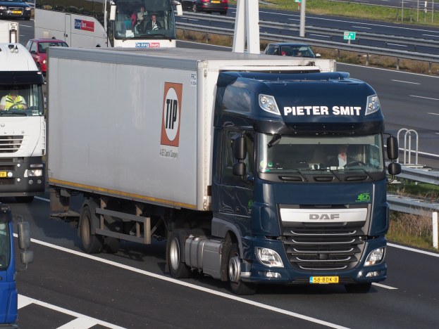 Eine Gruppe von Lastwagen fährt auf einer Autobahn, umgeben von Leitplanken, Pfählen, Schildern mit Text, Gras, Pflanzen und Bäumen, mit einem Wasserzeichen auf dem Bild.