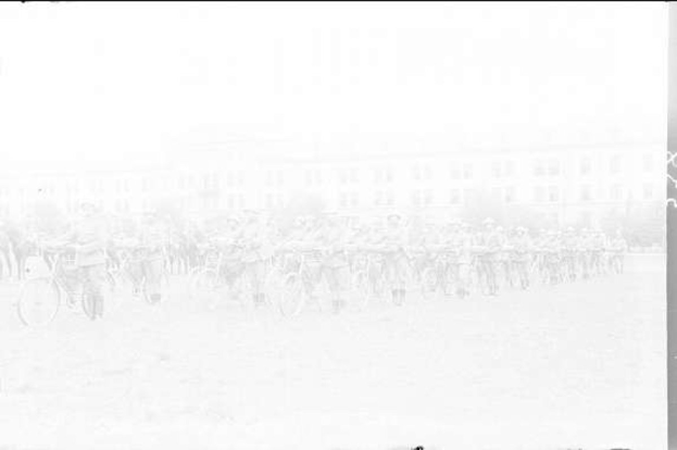 Schwarzes und weißes Foto von Radrennfahrern im Schnee an einem Gebäude im Hintergrund.