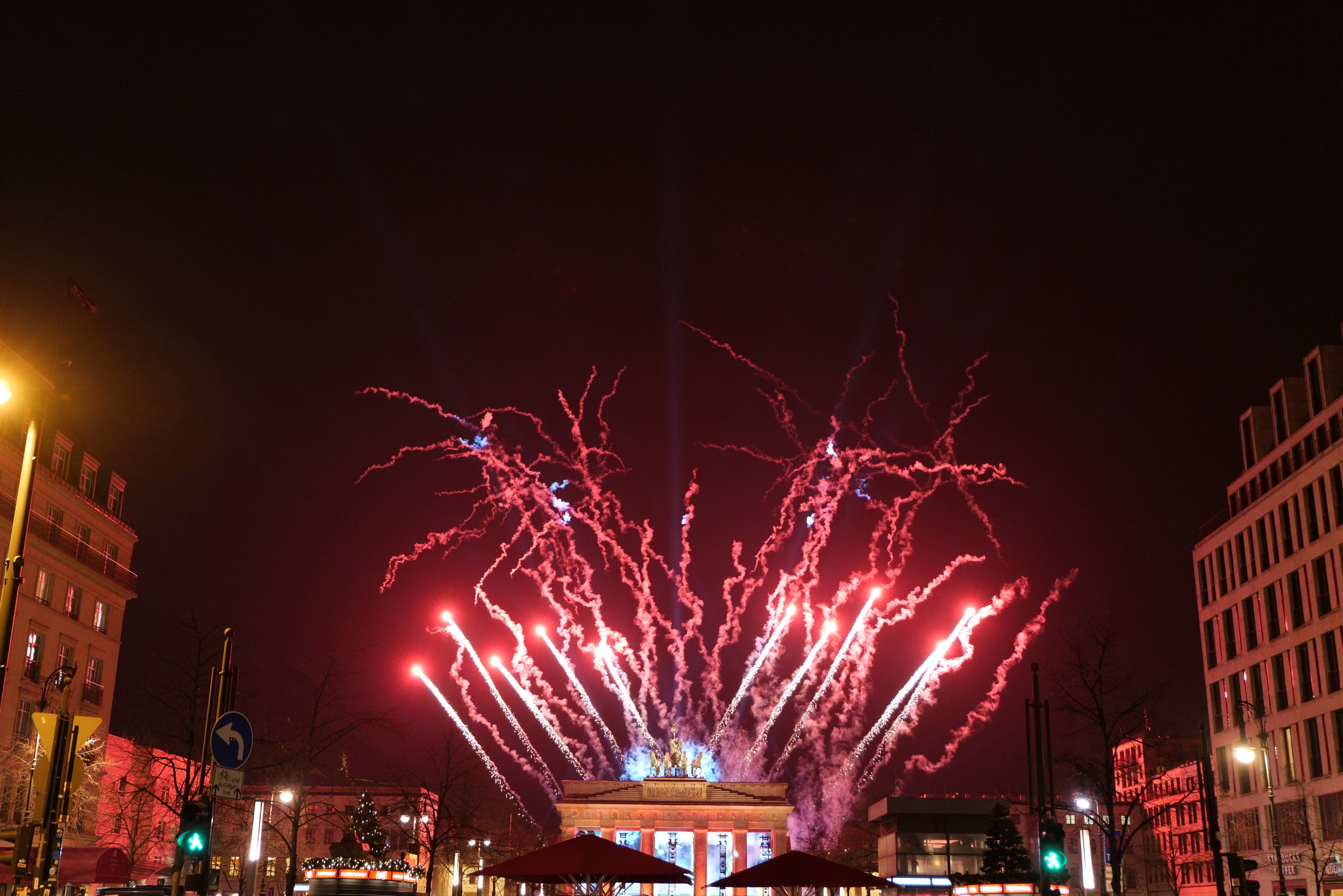 Eine belebte Stadtstraße am Silvesterabend in Berlin, voller Menschen, Fahrzeuge und Gebäude, beleuchtet von Lichtern und Feuerwerk am Himmel.