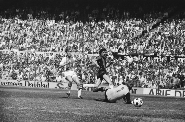 Schwarze und weiße Fotografie von Männern, die auf einem Feld Fußball spielen, mit Zuschauern im Hintergrund und einer Bundesliga 1978-79 Ajax 1-1 Hannover 96-Banner.