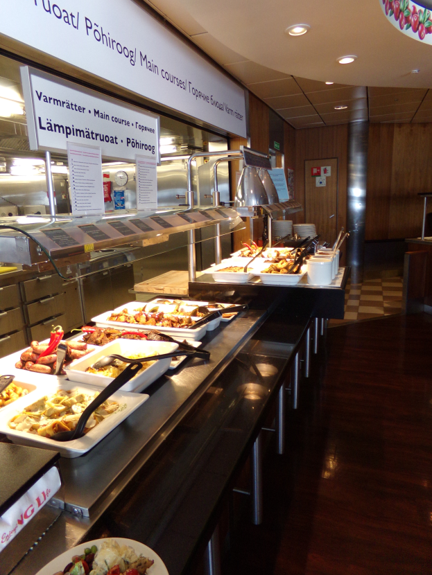 Ein Buffet mit verschiedenen Speisen, Servierutensilien, Namensschildern, Deckenleuchten und einer Wand im Hintergrund.