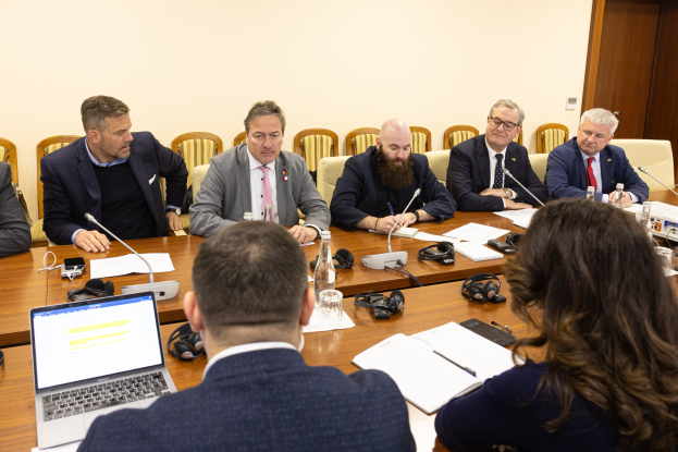 Eine Gruppe von Menschen, wahrscheinlich Mitglieder des Europäischen Parlaments, sitzt um einen Tisch in einem Konferenzraum, umgeben von Laptops, Büchern, Papieren, Flaschen, Gläsern, Headsets, Mikrofonen mit Ständern und Mobiltelefonen.