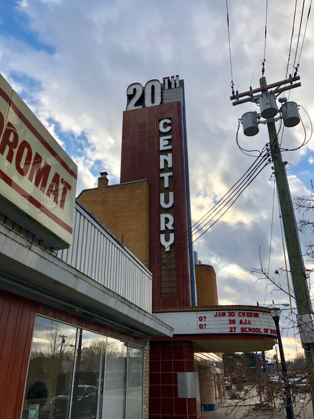 Das 20. Jahrhundert Theater in Detroit, Michigan, mit Glasw├Ąnden, Namensschildern, umgeben von B├Ąumen und Strommasten mit Dr├Ąhten unter einem bew├Âlktem Himmel.