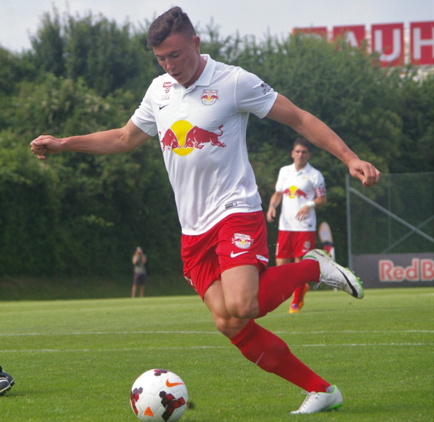 Ein professioneller Fußballspieler, der einen Ball auf einem Rasenfeld kickt, mit «RB Leipzig» im Hintergrund.