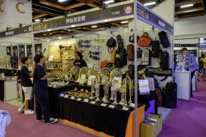 Gruppe von Menschen um einen Tisch mit Musikinstrumenten, Taschen und Schildern mit 'Hong Kong International Music Festival' Text, unter Deckenbeleuchtung mit Kartonbox auf dem Boden.