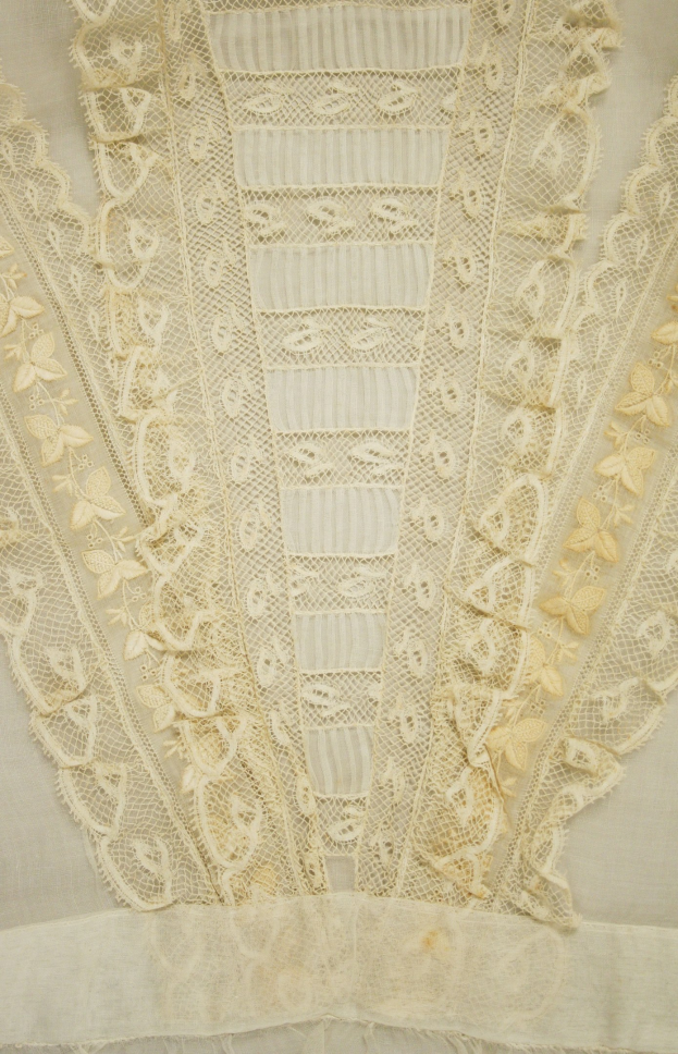 Nahaufnahme eines weißen Kleides mit zarter, kunstvoller Spitzenverzierung auf einem leichten, luftigen Stoff.