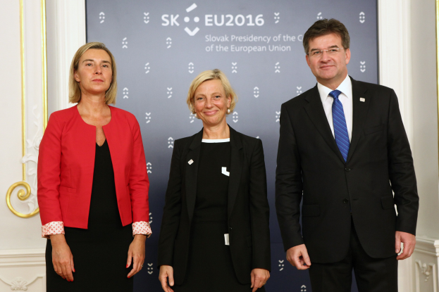 Zwei Frauen und ein Mann in formeller Kleidung stehen vor einem blauen und weißen Banner, auf dem "EU-Gipfel 2016: Die Europäische Union und die Europäische Kommission" steht, vor einer cremefarbenen Wand.