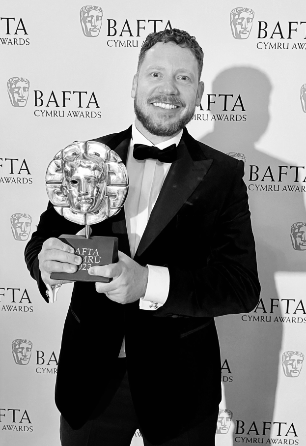 Mann in Smoking, der einen BAFTA-Award hält und vor einem "BAFTA Awards 2018"-Hintergrund steht.