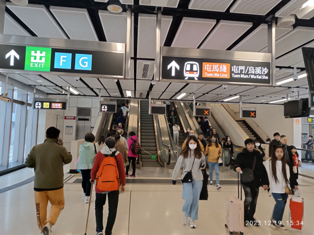 Menschen mit Gepäck durch einen geschlossenen Flughafen gehen, mit Rolltreppen, Informationsanzeigen, Deckenleuchten und Glaswänden im Hintergrund.