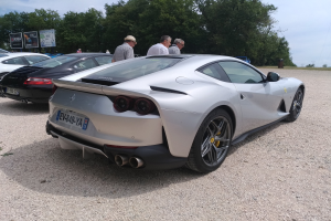 Roter Ferrari 812 Superfast beim Goodwood Festival of Speed, mit Zuschauern in Mützen und Veranstaltungsbeschilderung im Hintergrund.