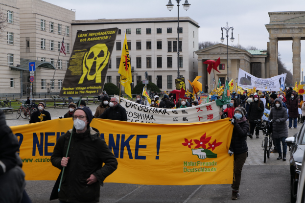 Eine große Gruppe von Menschen marschiert mit Schildern und Fahnen auf einer Straße, während Fahrzeuge auf der rechten Seite fahren, als Teil einer Demonstration gegen Atomkraft in Deutschland.