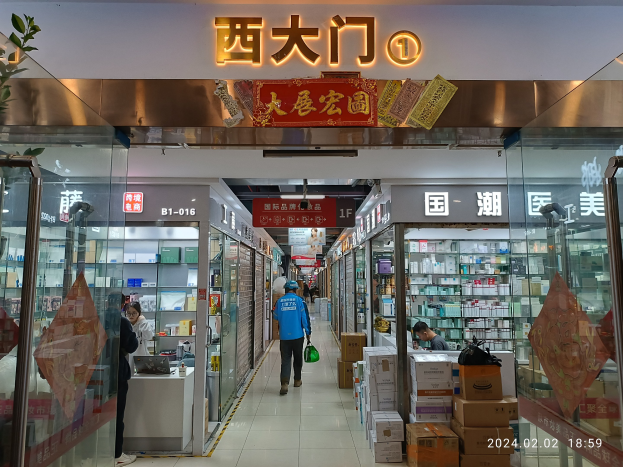 Innenraum einer chinesischen Apotheke mit Glaswänden, Regalen voller Artikel, verstreuten Kartons, einer Pflanze auf der linken Seite und einem Namensschild oben.